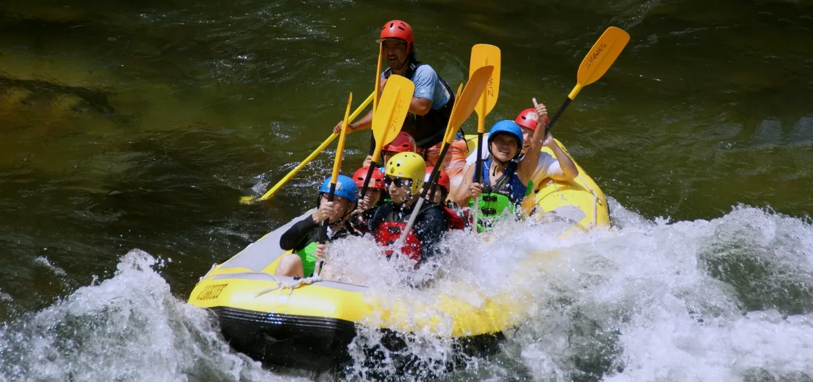 みなかみのホワイトウォーターラフティング。家族グループがガイドとともに川の波を進む日本のアウトドアアクティビティ, Exciting Minakami whitewater rafting in Japan with a family group paddling through river waves on a guided outdoor adventure.