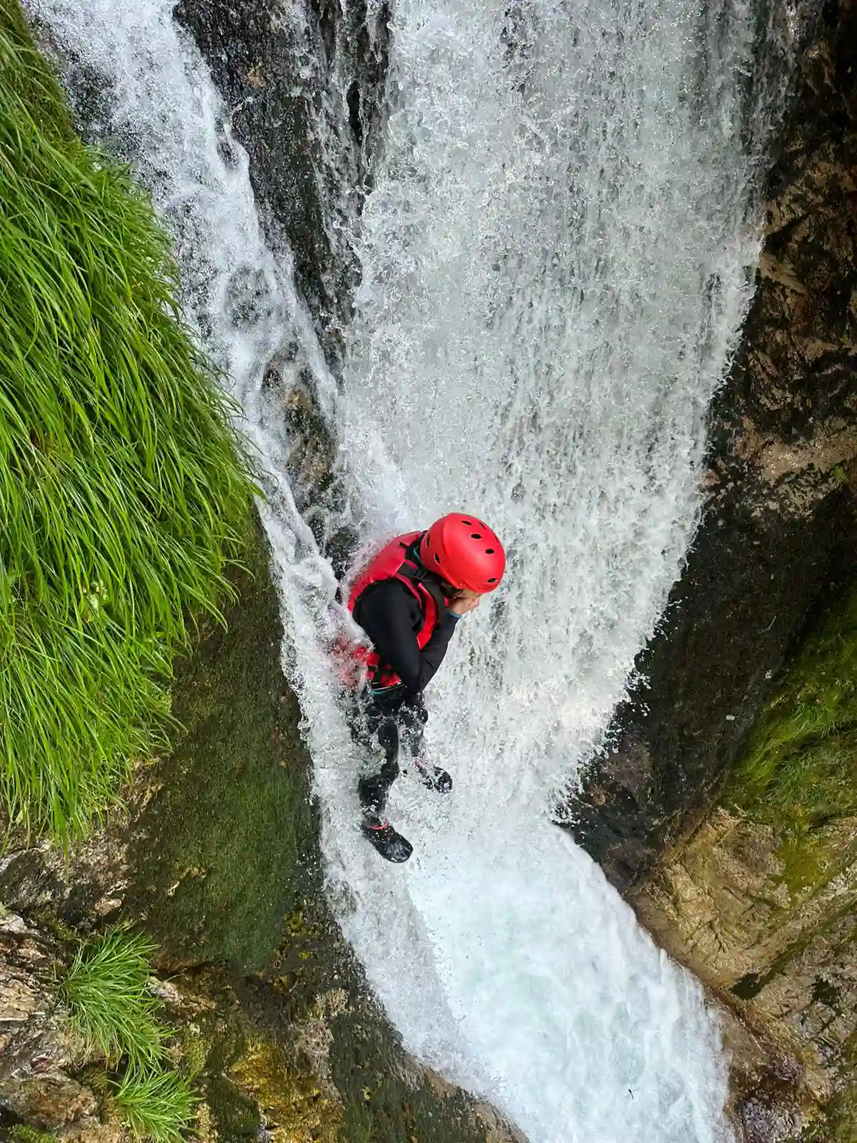 (水上)みなかみキャニオニング冒険者がスリル満点のみなかみ半日キャニオニングツアー中に天然の滝のシュートを滑り降りる,Minakami canyoning adventurer sliding down natural waterfall chute during thrilling minakami half day canyoning tour.